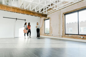 The mid adult female real estate agent shows two businesswomen an open loft in the city used for office space.